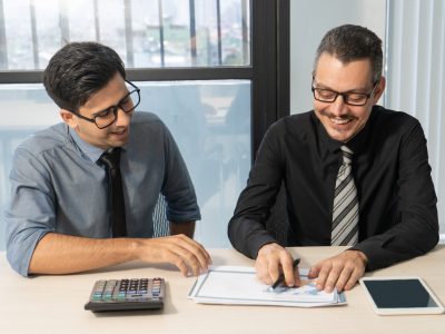 Jolly business partners discussing sales development at meeting. Happy excited businessmen examining papers and enjoying teamwork in office. Report concept